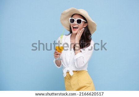Beautiful smiling Asian woman in summer outfit with a glass of orange juice isolated on colorful blue background. Royalty-Free Stock Photo #2166620517