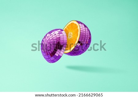 Cut disco ball as an orange, floating in the air on a green background.  Royalty-Free Stock Photo #2166629065