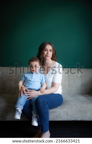 Mother and son seated on couch in front of green backdrop