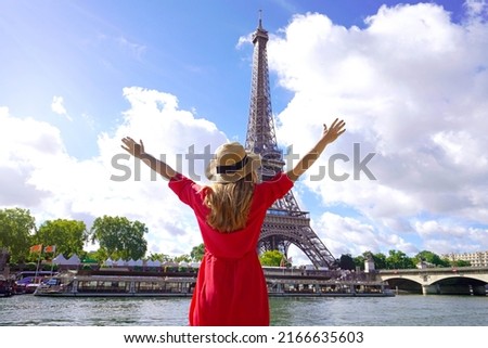 Woman traveler with hat and arms raised on the Seine River in Paris. Back view of fashion woman with open arms in Paris beautiful view with Eiffel Tower on the background.