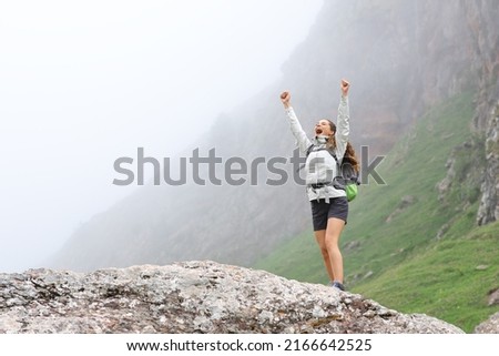 Excited trekker raising arms celebrating success in the mountain a foggy day Royalty-Free Stock Photo #2166642525