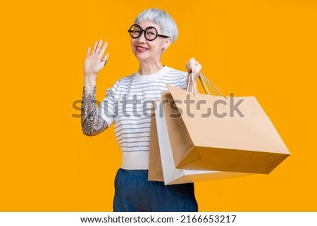 Asian happy senior female woman tattoo holds colourful shopping packages standing on yellow background studio shot, Close up Portrait old female hand hold shopping bags enjoy shopping with joyful