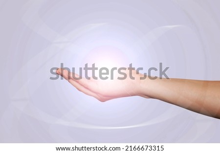 Close-up of the hand of a young woman holding a light ball isolated on a gray-blue background. Spirituality, awakening, enlightenment