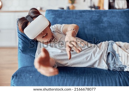 Young Asian guy wearing VR glasses and lying on couch at home
