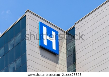 The blue and white letter H sign on a modern hospital building