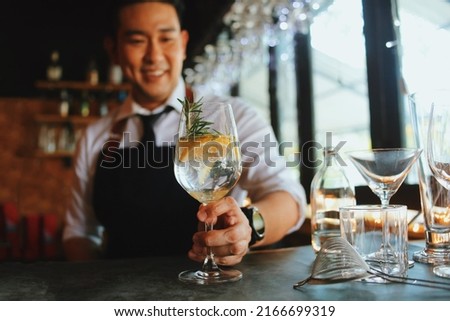 Handsome male bartender in apron preparing drink for customer at bar counter. Asian bartender man making some drink for guest of hotel. Royalty-Free Stock Photo #2166699319