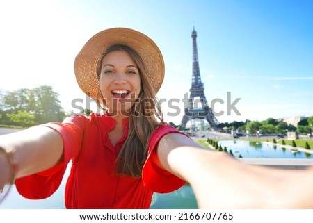 Excited fashion woman with red dress and hat has fun making self portrait with Eiffel Tower on the background in Paris, France.