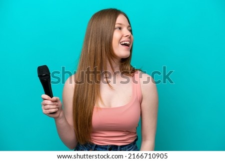 Singer caucasian woman picking up a microphone isolated on blue background laughing in lateral position