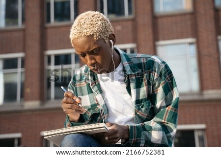 Portrait of pensive man artist    drawing something, listening music relaxing outdoors sitting alone on the street. Student studying, taking notes, education concept 