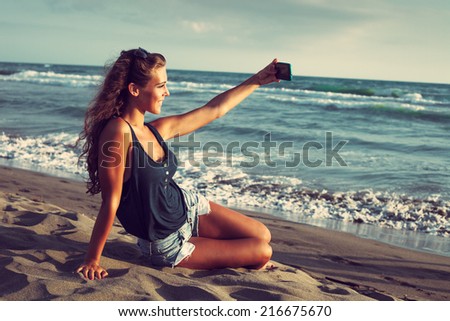smiling young woman take a selfie photo at sandy beach by the sea at sunset