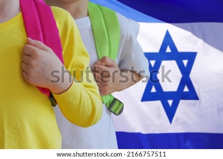 Two children with satchels background of Israel flag. Concept of upbringing and educating children in Israel