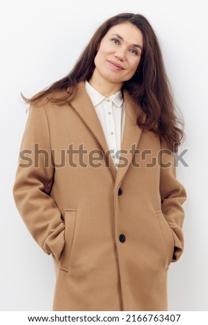 beautiful, sweet, joyful woman with dark hair in a stylish beige coat. vertical photo on a light background