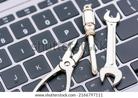 Computer hardware service and maintenance concept : Open-end wrench, a screwdriver, a needle-nose plier on a computer keyboard, depicts repairing, software updating or changing to a newer version. Royalty-Free Stock Photo #2166797111