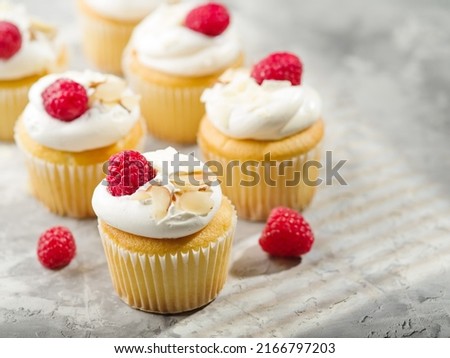 Many delicious muffins with whipped cream, fresh raspberries and almond slices on a white background. Festive composition. Birthday, banquet. Restaurant, hotel, cafe, deli, confectionery.