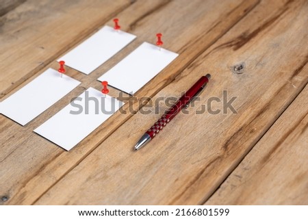 Blank business cards and a pen against a wooden background. Four white paper rectangles were pinned with push pins to old boards. Selective focus.