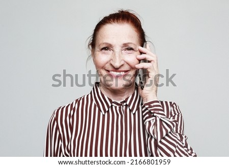 Elderly smiling happy woman 70s wear striped shirt talk speak on mobile cell phone conducting pleasant conversation isolated on grey background. People lifestyle concept.