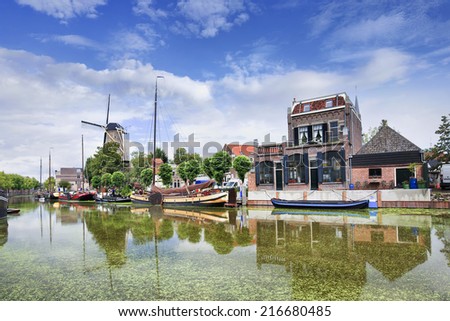 Smooth green canal with moored boats and monumental houses in the old town of Gouda, The Netherlands. Royalty-Free Stock Photo #216680485