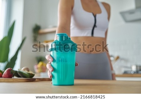 Close-up of woman in sports clothing holding shaker with protein cocktail at the kitchen Royalty-Free Stock Photo #2166818425