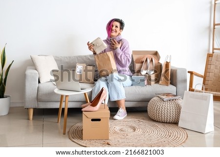 Beautiful woman with new bag sitting on sofa at home. Online shopping