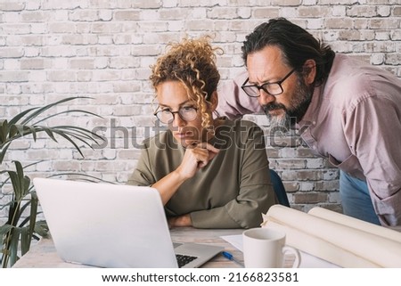 Man and woman working together on laptop in home office at the table desk. People and online digital job business. Adult couple looking with concentration on computer working. Concept of modern life Royalty-Free Stock Photo #2166823581