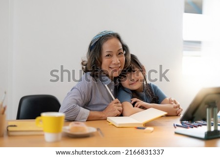 Smiling senior grandma and cute little kid granddaughter watching cartoons on laptop together, happy older grandmother grawing and painting.