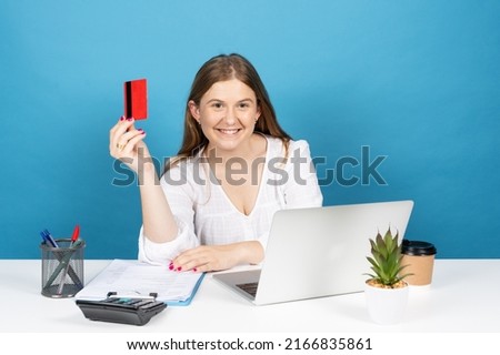 Pretty office worker woman holding credit card and looking at camera isolated on blue background. Online shopping concept