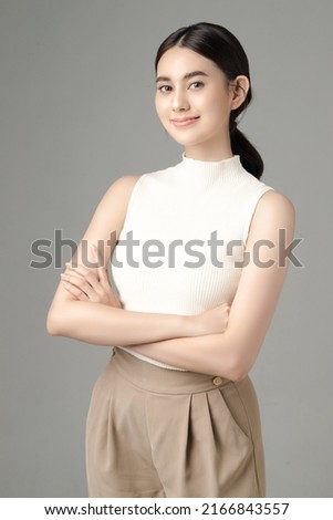 Confident Asian woman crossing her arms and looking at camera isolated on gray background. Portrait of a beautiful girl in the studio.
