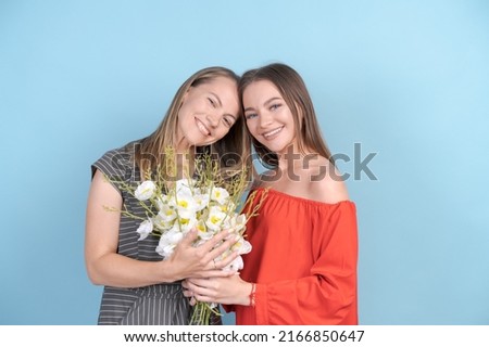 Happy women's day. Beloved daughter congratulates her mother and gives her beautiful flowers in a bouquet. Mom and girl smile and hug on a blue background. Family holiday and unity.