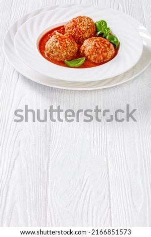 Italian Porcupine Balls, ground beef and rice meatballs in tomato sauce with basil leaves in white bowl on white wooden table, vertical view from above, free space