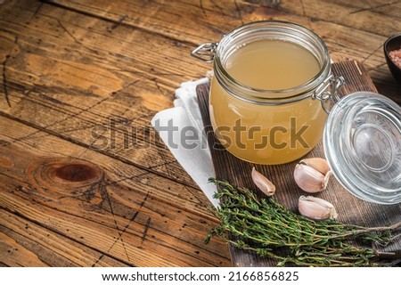 Bone broth for chicken soup in a glass jar. Wooden background. Top view. Copy space.