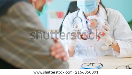 close up of asian female doctor wearing face mask is showing eyeball model and explaining about eyes disease to elder senior man patient in hospital Royalty-Free Stock Photo #2166858391