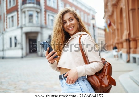 Young woman messaging on phone outside. Beautiful woman smiles sincerely and walks outdoors. Fashion style.