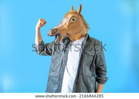 Funny horse head on human body on a green shirt on blue background, strong and win symbol . Clip art, negative space.