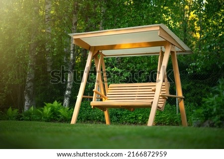 Wooden swing in the green garden. Recreation in the park. Garden design. Relax in the fresh air. Garden furniture made of wood. Royalty-Free Stock Photo #2166872959