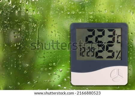 Digital hygrometer with thermometer on glass with water drops. Space for text Royalty-Free Stock Photo #2166880523