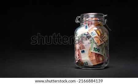 Glass jar with euro currency savings on black background