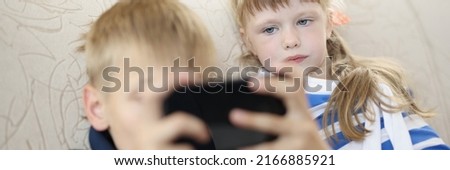 Brother and sister at home on sofa watching on smartphone screen