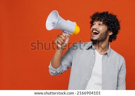 Jubilant overjoyed excited vivid young bearded Indian man 20s years old wears blue shirt hold scream in megaphone announces discounts sale Hurry up isolated on plain orange background studio portrait Royalty-Free Stock Photo #2166904101