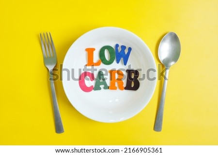 Low carb diet concept. Flat lay composition of low carbohydrates word text in plate with eating utensils spoon and fork in bright yellow background. Royalty-Free Stock Photo #2166905361