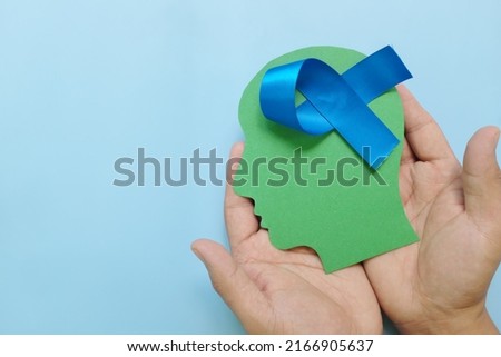 Hand holding human head profile with blue awareness ribbon on brain. Prostate cancer, colon and colorectal cancer, peace, alopecia and arthritis care concept.