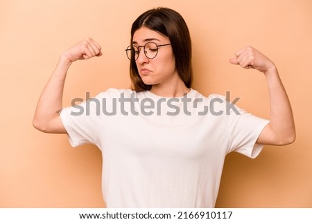 Young hispanic woman isolated on beige background showing strength gesture with arms, symbol of feminine power