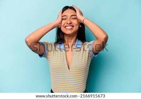 Young hispanic woman isolated on blue background laughs joyfully keeping hands on head. Happiness concept.