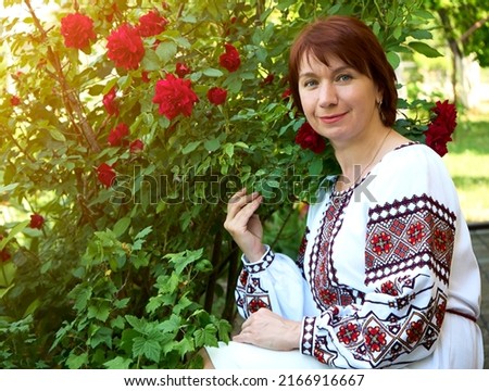 Gorgeous ukrainian woman in traditional embroidery vyshyvanka dress sitting near flowers on nature forest background. Ukraine, culture, freedom, national costume.
