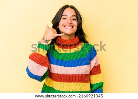 Young hispanic woman isolated on yellow background showing a mobile phone call gesture with fingers.