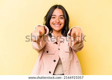 Young hispanic woman isolated on yellow background cheerful smiles pointing to front.
