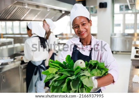portrait young teen girl cook student. Cooking class. culinary classroom. happy young african woman students holding fresh vegetables for cooking in cooking school.  Royalty-Free Stock Photo #2166937995