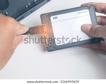 Put your hand on the cable to install the square SSD. To the PC there are two cables, a power cable and a data cable. It is a new technology, SATA III 6GB per s. Royalty-Free Stock Photo #2166943659