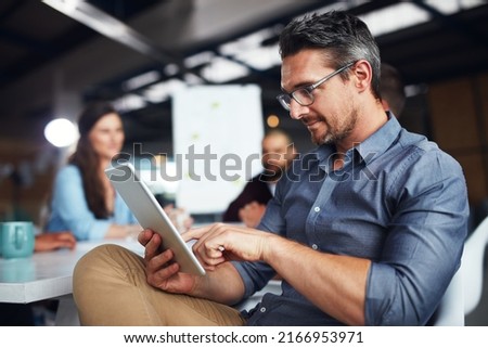 The creative process. Shot of a man sitting at a table in an office using a digital tablet with colleagues working in the background. Royalty-Free Stock Photo #2166953971