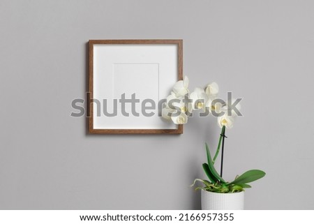 Square wooden frame mockup with white orchid flowers in pot over grey wall