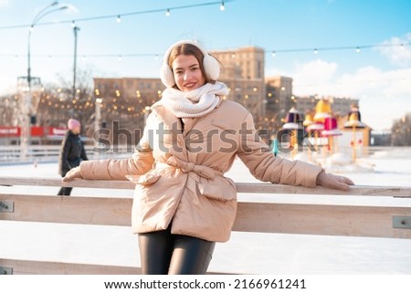 Beautiful lovely young adult woman brunet hair warm winter jackets stands near ice skate rink background Town Square. Christmas mood lifestyle Happy holiday woman walk snowy day Winter leisure